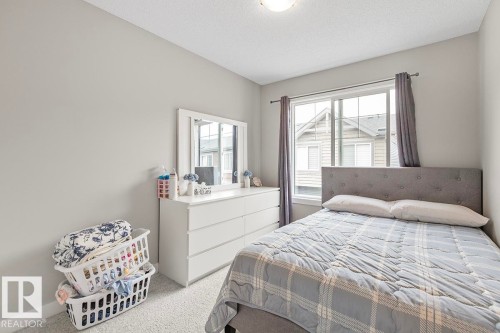 Bright bedroom featuring a large window, plush carpet flooring, and a textured headboard - #22 3025 151 Av Nw, Edmonton, AB - Indoor Photo Showing Bedroom