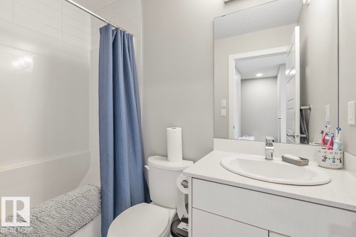 Bathroom featuring a white vanity with an undermount sink, a large mirror, a toilet, a bathtub with a shower, and light gray wall paint - #22 3025 151 Av Nw, Edmonton, AB - Indoor Photo Showing Bathroom