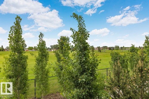 Expansive green space featuring a chain-link fence, mature trees, and a clear blue sky with white clouds - #22 3025 151 Av Nw, Edmonton, AB - Outdoor With View