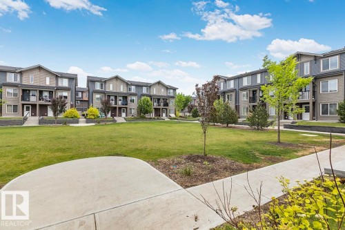 Central greenspace featuring expansive lawn areas and mature plantings - #22 3025 151 Av Nw, Edmonton, AB - Outdoor With Facade