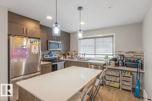 Modern kitchen featuring a central island with white countertop, recessed lighting, and two pendant fixtures - #22 3025 151 Av Nw, Edmonton, AB - Indoor Photo Showing Kitchen With Stainless Steel Kitchen With Upgraded Kitchen