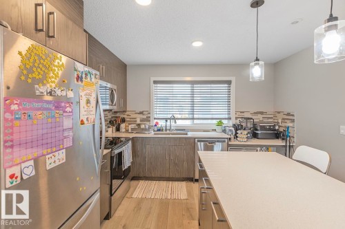 Modern kitchen featuring stainless steel appliances, light wood-finish flooring, and a stone-look island countertop - #22 3025 151 Av Nw, Edmonton, AB - Indoor Photo Showing Kitchen