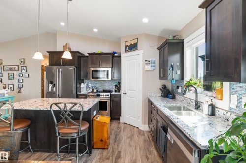 Kitchen featuring dark wood-finish cabinetry, stainless steel appliances, speckled stone countertops, and a tile backsplash - 4927 57 Avenue, Cold Lake, AB 
