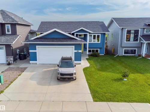 Contemporary residential structure featuring a blue exterior, attached garage, concrete driveway, and a front lawn with a young tree - 4927 57 Avenue, Cold Lake, AB 
