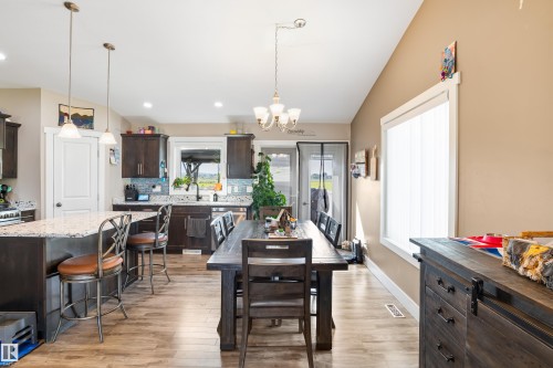 Open-concept kitchen and dining area featuring wood-finish flooring, dark wood cabinetry, a light-colored island countertop, and recessed lighting - 4927 57 Avenue, Cold Lake, AB 