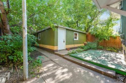 Detached shed with an exterior door and single window, a concrete path, a wood fence, and mature trees - 