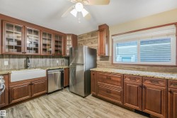 Kitchen featuring wood-finish flooring, wood cabinetry with glass-front uppers, granite countertops, stainless steel appliances, and a farmhouse sink - 