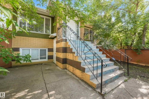 Split-level exterior featuring brick and stucco finishes, concrete steps with decorative wrought iron railings, and mature surrounding trees - 9347 105 Avenue Nw, Edmonton, AB 