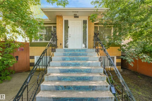 Brick exterior with a white entry door, wrought iron railings, and concrete stairs - 9347 105 Avenue Nw, Edmonton, AB 