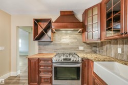 Wood-finish cabinetry, stainless steel range, farmhouse-style sink, granite-style countertop, and wood-finish backsplash - 