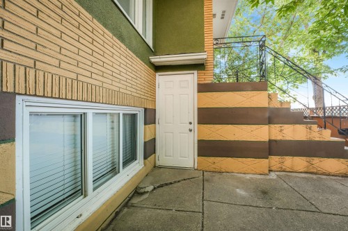 Brick and stucco exterior with a white entry door, ground-level windows, and concrete paving - 9347 105 Avenue Nw, Edmonton, AB 