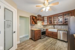 Kitchen featuring wood-finish flooring, a farmhouse sink, stainless steel appliances, granite countertops, and a decorative pantry door - 