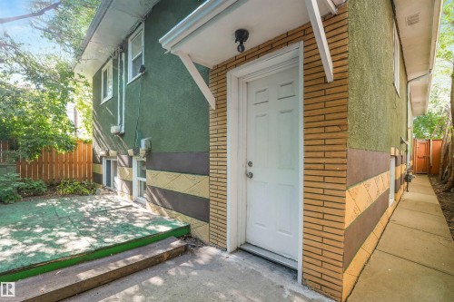 Exterior wall featuring textured green stucco, decorative yellow and brown patterned paneling, and a white paneled door - 9347 105 Avenue Nw, Edmonton, AB 