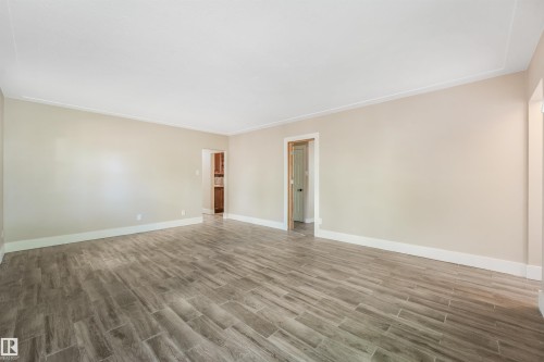 Spacious room featuring wood-finish tile flooring, neutral wall paint, white trim, and crown molding - 9347 105 Avenue Nw, Edmonton, AB 