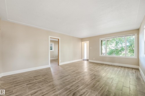 Spacious interior featuring wood-look tile flooring, neutral wall tones, and a large picture window - 9347 105 Avenue Nw, Edmonton, AB 