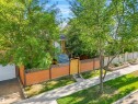 Lush mature trees framing the property, wooden gate entrance, paved sidewalk, concrete curb, and a garage door - 9347 105 Avenue Nw, Edmonton, AB 