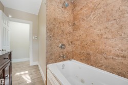 Tiled shower surround with integrated tub, chrome fixtures, and wood-finish flooring - 