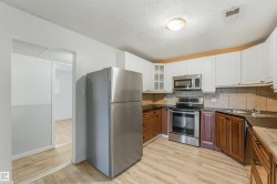 Kitchen featuring wood-finish flooring, two-tone cabinetry, stainless steel appliances, a tile backsplash, and dark countertops - 