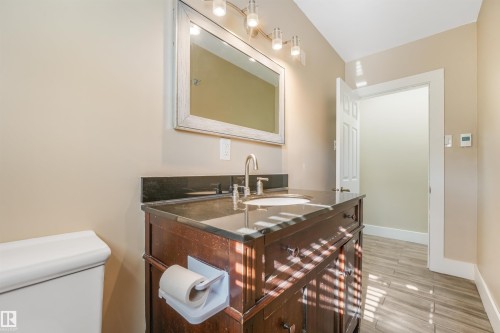 Wood-finish vanity with an undermount sink, dark stone countertop, and brushed nickel faucet - 9347 105 Avenue Nw, Edmonton, AB 