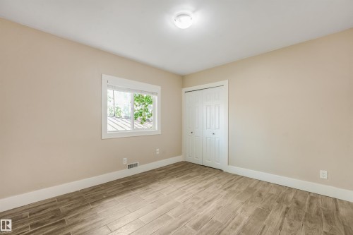 Neutral wall paint, wood-finish flooring, white window trim, white bi-fold closet doors, and a ceiling-mounted light fixture - 9347 105 Avenue Nw, Edmonton, AB 
