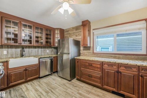 Kitchen featuring wood-finish flooring, wood cabinetry with glass-front uppers, granite countertops, stainless steel appliances, and a farmhouse sink - 9347 105 Avenue Nw, Edmonton, AB 
