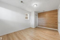 Wood-finish accent wall, wood-finish flooring, white painted walls, white trim, and a window with blinds - 