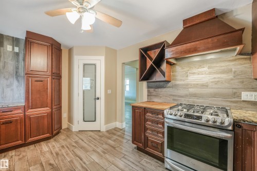 Stainless steel range with a built-in hood, wood-finish cabinetry, wood-finish flooring, wood-finish backsplash, and a ceiling fan - 9347 105 Avenue Nw, Edmonton, AB 
