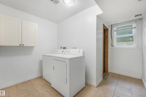 White shaker-style cabinetry with gold-toned hardware, light-toned tiled flooring, and a single window with blinds - 9347 105 Avenue Nw, Edmonton, AB 