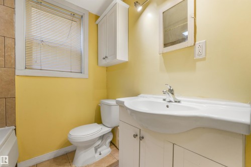 White vanity with integrated sink, chrome faucet, wall-mounted mirror, and tile flooring - 9347 105 Avenue Nw, Edmonton, AB 