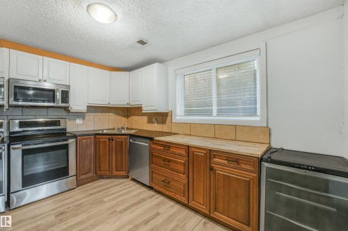 Kitchen featuring stainless steel appliances, wood-finish flooring, white upper cabinetry, and wood lower cabinetry - 9347 105 Avenue Nw, Edmonton, AB 