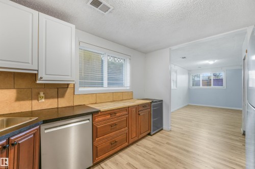 Kitchen featuring wood-finish flooring, two-tone cabinetry, and a tile backsplash - 9347 105 Avenue Nw, Edmonton, AB 
