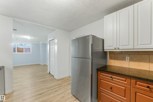 Kitchen area with white upper cabinetry, wood-finish lower cabinetry, a stainless steel refrigerator, and dark countertops - 9347 105 Avenue Nw, Edmonton, AB 