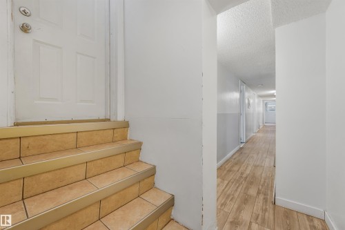 Tile stairs with metal tread, white door, and wood-finish flooring in the hallway - 9347 105 Avenue Nw, Edmonton, AB 