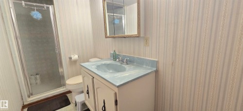Built-in vanity with a light blue countertop, inset sink, chrome faucet, and cabinet storage - 4713 55 Avenue, Vegreville, AB 