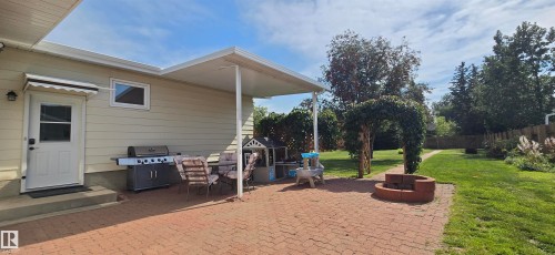 Expansive backyard featuring a brick paver patio, covered porch area, and a built-in fire pit - 4713 55 Avenue, Vegreville, AB 