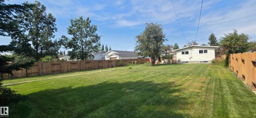 Expansive backyard featuring a large grass area, mature trees, and wood fencing - 4713 55 Avenue, Vegreville, AB 