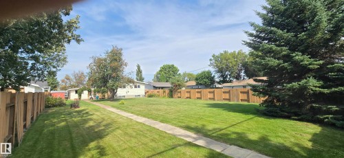 Expansive backyard featuring a manicured lawn, established trees, a concrete pathway, and perimeter fencing - 4713 55 Avenue, Vegreville, AB 