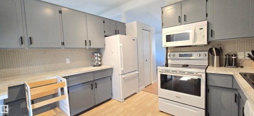 Kitchen featuring gray cabinetry, light wood-finish flooring, white appliances, and a tiled backsplash - 4713 55 Avenue, Vegreville, AB 