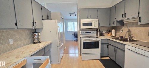 Kitchen featuring light gray cabinetry with black hardware, white appliances, light-toned countertop, and light-toned tile backsplash - 4713 55 Avenue, Vegreville, AB 