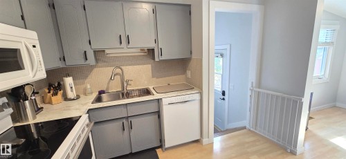 Kitchen featuring gray cabinetry with black hardware, double basin stainless steel sink, tiled backsplash, and light-toned flooring - 4713 55 Avenue, Vegreville, AB 