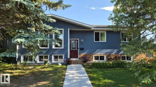 Blue siding exterior with white window frames, a red front door, a concrete walkway, and a landscaped front yard - 5201 56A Street, Beaumont, AB 