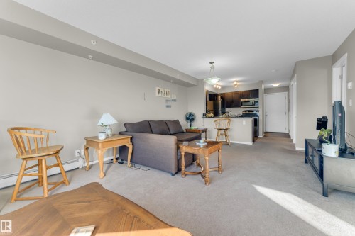 Open-concept living space with carpeted flooring, neutral wall tones, recessed lighting, and a kitchen island with dark cabinetry - #430 3315 James Mowatt Tr Sw, Edmonton, AB 