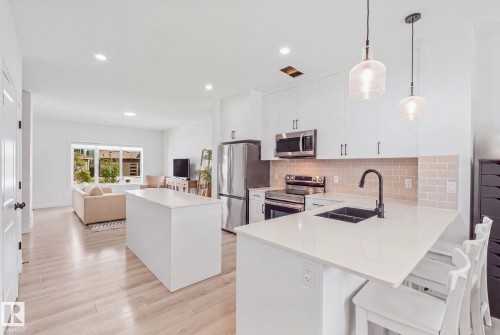 Modern kitchen featuring white cabinetry, stainless steel appliances, a tile backsplash, and an island with counter seating - 4023 Hawthorn Link Link Sw, Edmonton, AB 