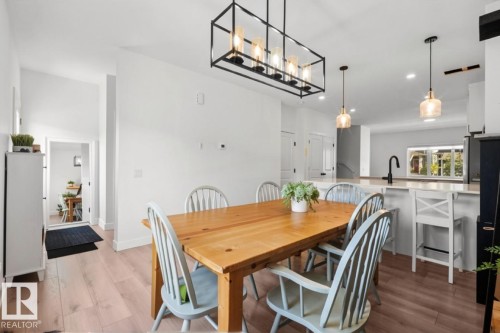Open-concept dining area featuring wood-finish flooring, a linear chandelier, and a breakfast bar with pendant lighting - 4023 Hawthorn Link Link Sw, Edmonton, AB 