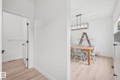 Light wood-finish flooring, white walls, and a linear black-framed chandelier - 4023 Hawthorn Link Link Sw, Edmonton, AB 