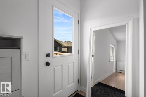 White paneled door with glass insert, matte black hardware, and an adjacent light switch - 4023 Hawthorn Link Link Sw, Edmonton, AB 