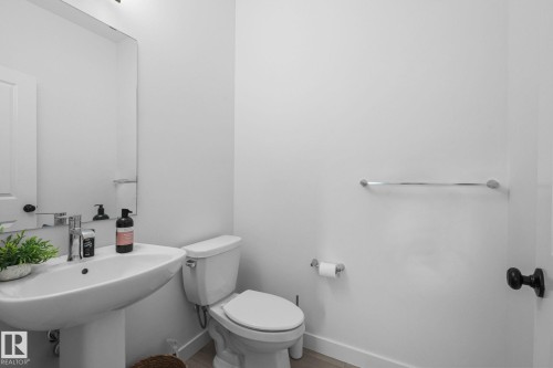 Pedestal sink with chrome faucet, toilet, wall-mounted mirror, and wood-finish flooring - 4023 Hawthorn Link Link Sw, Edmonton, AB 
