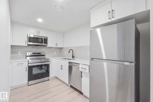 Modern kitchen featuring stainless steel appliances, white cabinetry, light-toned countertops, and a tiled backsplash - 4023 Hawthorn Link Link Sw, Edmonton, AB 