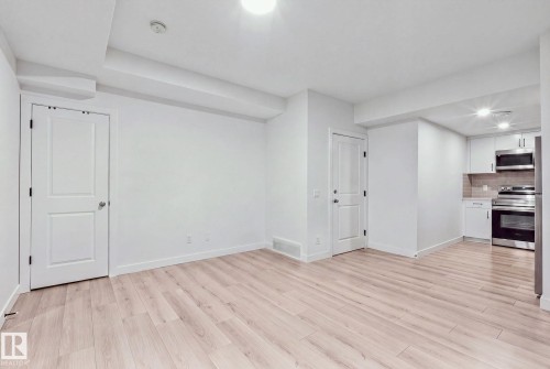 Open-concept living space featuring wood-finish flooring, recessed lighting, white walls, and a contemporary kitchen with stainless steel appliances - 4023 Hawthorn Link Link Sw, Edmonton, AB 