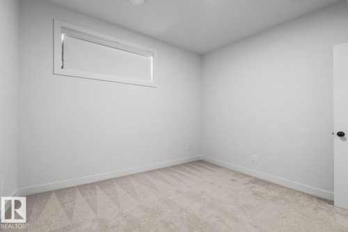 Bright secondary bedroom featuring neutral wall finishes, a high transom window providing natural light, and neutral carpeting - 4023 Hawthorn Link Link Sw, Edmonton, AB 